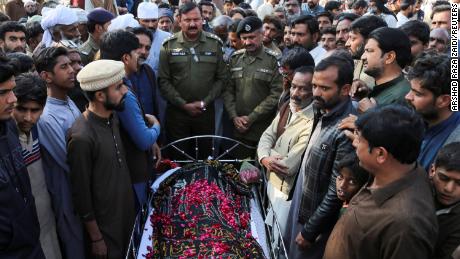Mensen staan ​​naast het lichaam van een man die volgens de politie standrechtelijk werd geëxecuteerd door een menigte, in het dorp Tulamba, centraal Pakistan, op 13 februari 2022.