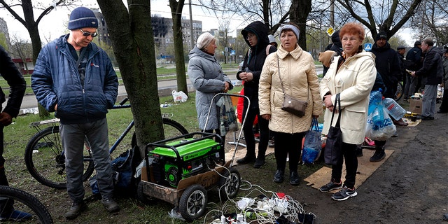 Lokale bewoners verzamelen zich bij een generator om hun mobiele apparaten op te laden in een gebied dat wordt gecontroleerd door door Rusland gesteunde separatistische troepen in Mariupol, Oekraïne, vrijdag 22 april 2022 (AP Photo/Alexei Alexandrov)
