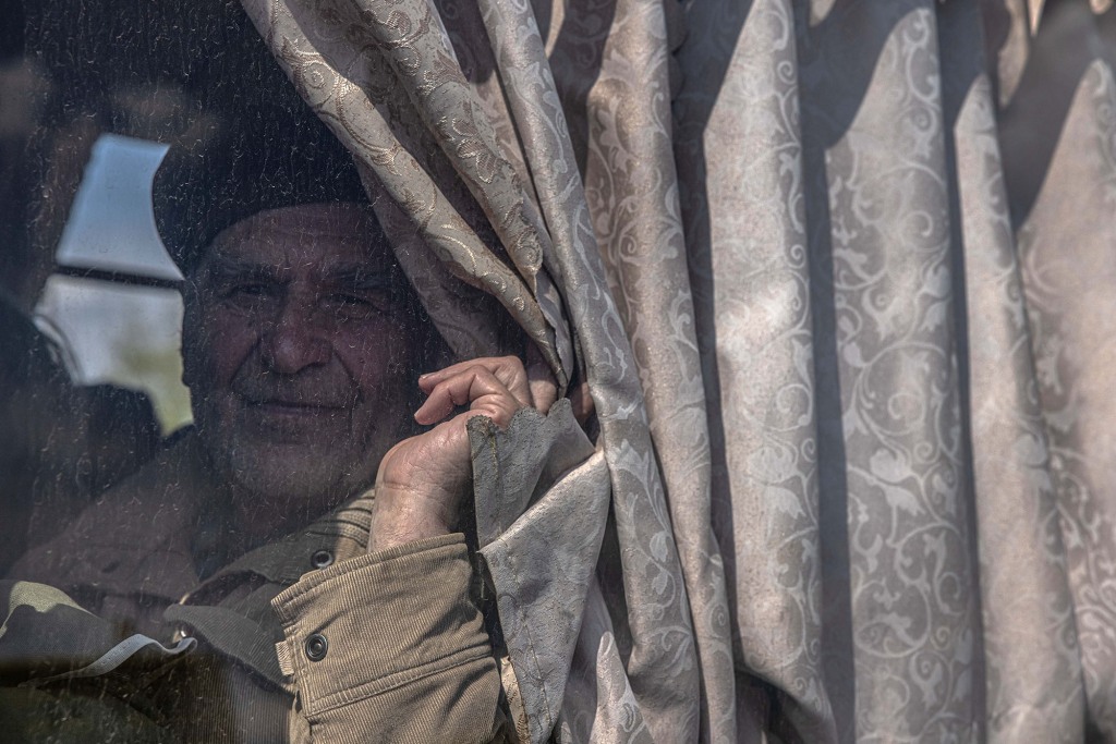 Een oudere man kijkt naar hem terwijl hij in een bus zit na aankomst uit de frontliniestad Urekiev, op het evacuatiepunt in Zaporizhia, Oekraïne