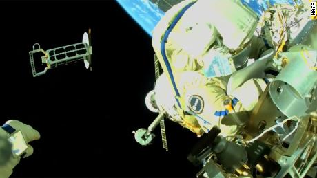 Cristoforetti is te zien aan de buitenkant van het internationale ruimtestation ISS terwijl Artemyev, wiens hand linksonder wordt getoond, een nanosatelliet in een baan om de aarde gooit. 