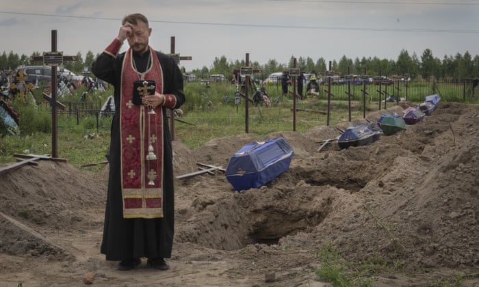 Een priester bidt voor niet-geïdentificeerde burgers die zijn gedood door Russische troepen in Bucha.