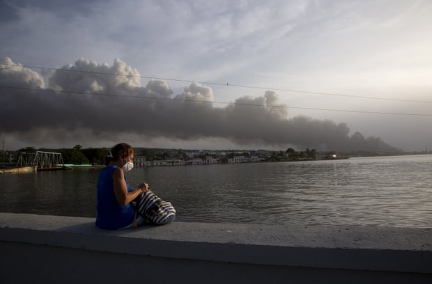 Een bewoner zit op de Malecon-zeewering terwijl op de achtergrond rook opstijgt van het vuur.