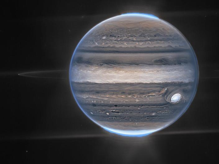 Wijds beeld van Jupiter, gemaakt door Webb.  De wazige plekken in de lagere achtergrond zijn waarschijnlijk sterrenstelsels.