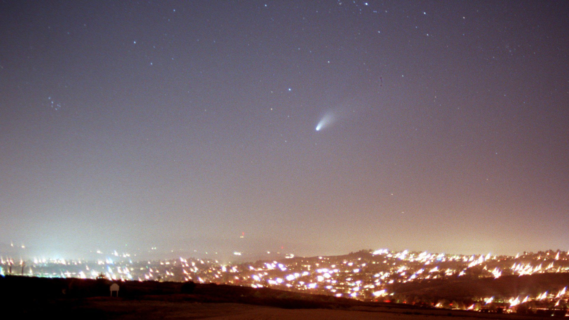 Een heldere komeet boven een helder veld van stadslichten