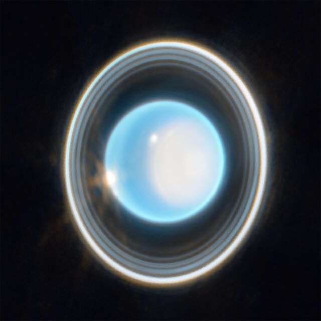 Planeet Uranus op een zwarte achtergrond.  De planeet lijkt lichtblauw, met een grote witte vlek aan de rechterkant.  Aan de rand van die plek linksboven zit een helderwitte vlek.  Er is nog een witte vlek aan de linkerkant van de planeet om 9 uur.Rond de planeet is een systeem van overlappende ringen.  Uranusringen zijn verticaal.