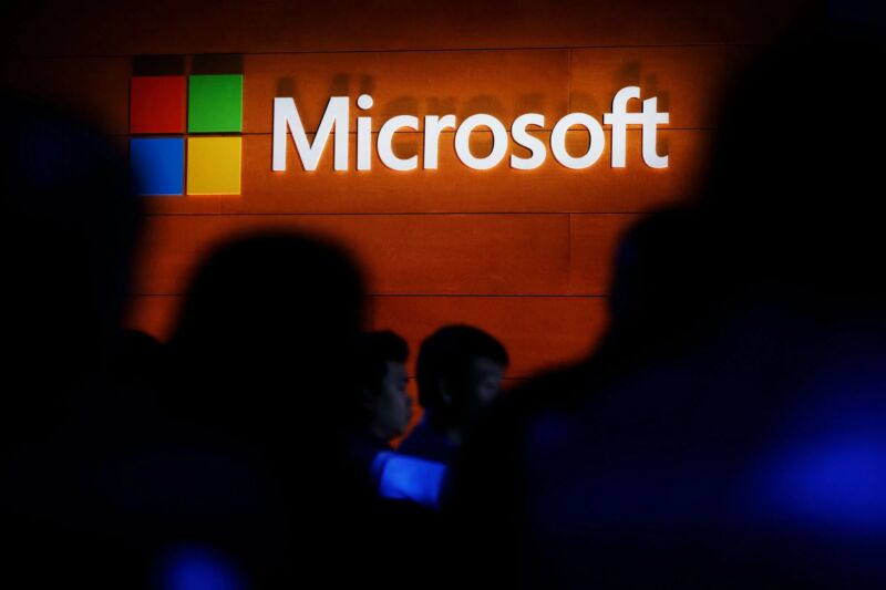 De silhouetten staan ​​onder het Microsoft-logo op een muur van imitatiehout.