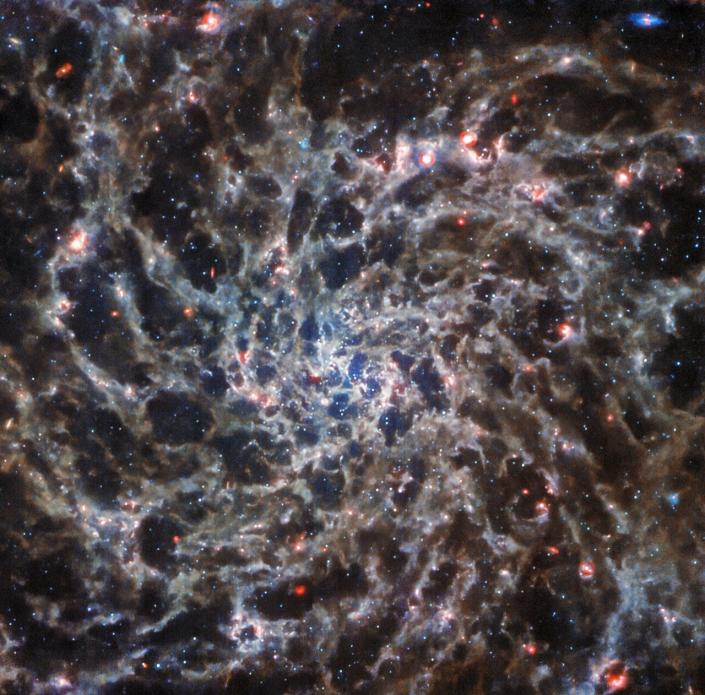 Afbeelding van een spiraalstelsel van de James Webb Space Telescope.  De spiralen zien eruit als spinnenwebben met overal in het beeld roze gasachtige gebieden.