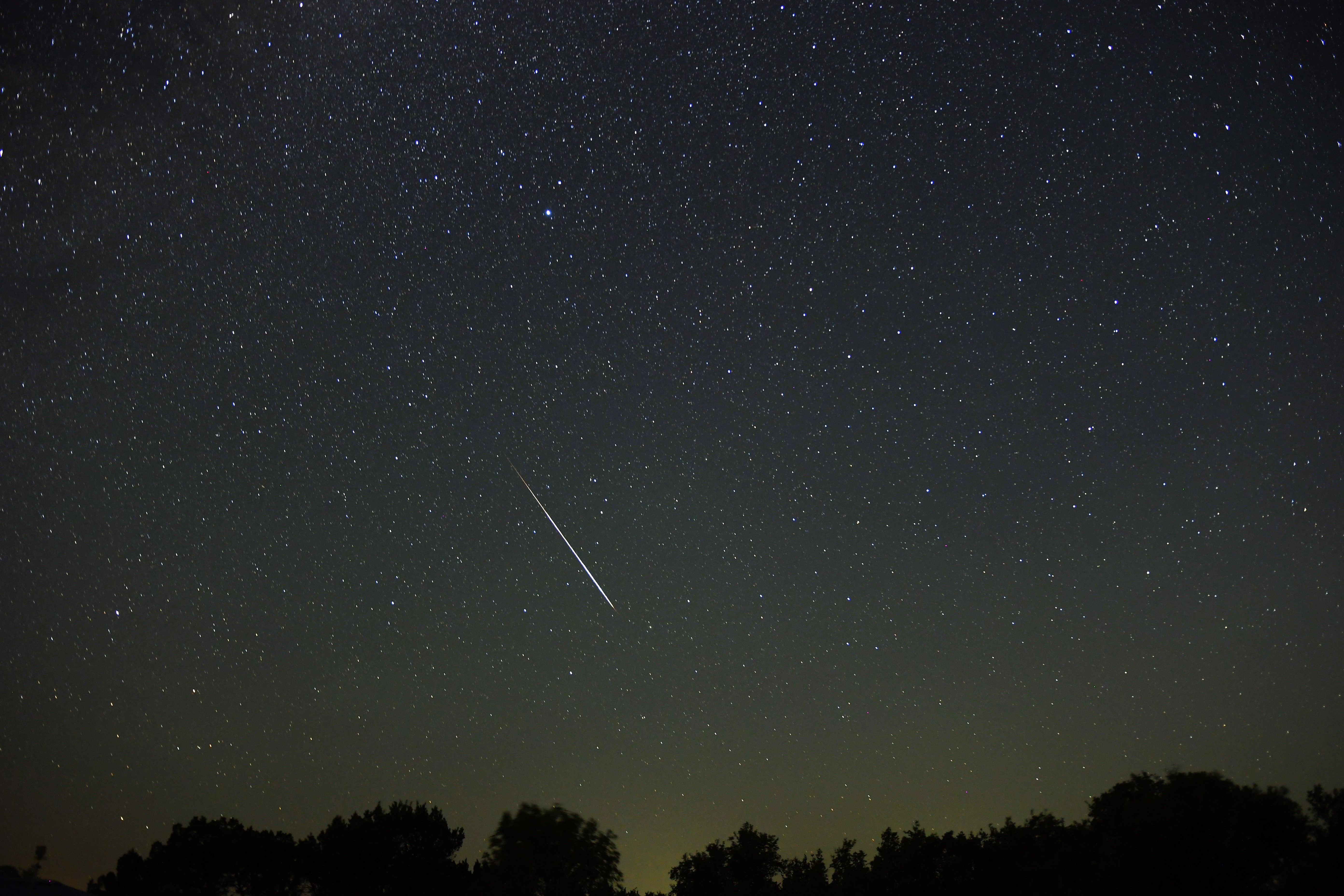 Een meteorenregen wordt afgebeeld tegen een sterrenhemel en een schilderachtige voorgrond