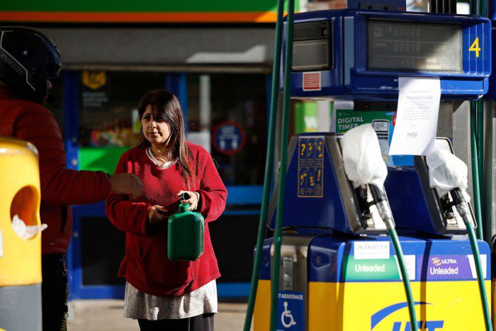 Een vrouw draagt ​​een blikje benzine in Leyton, Oost-Londen