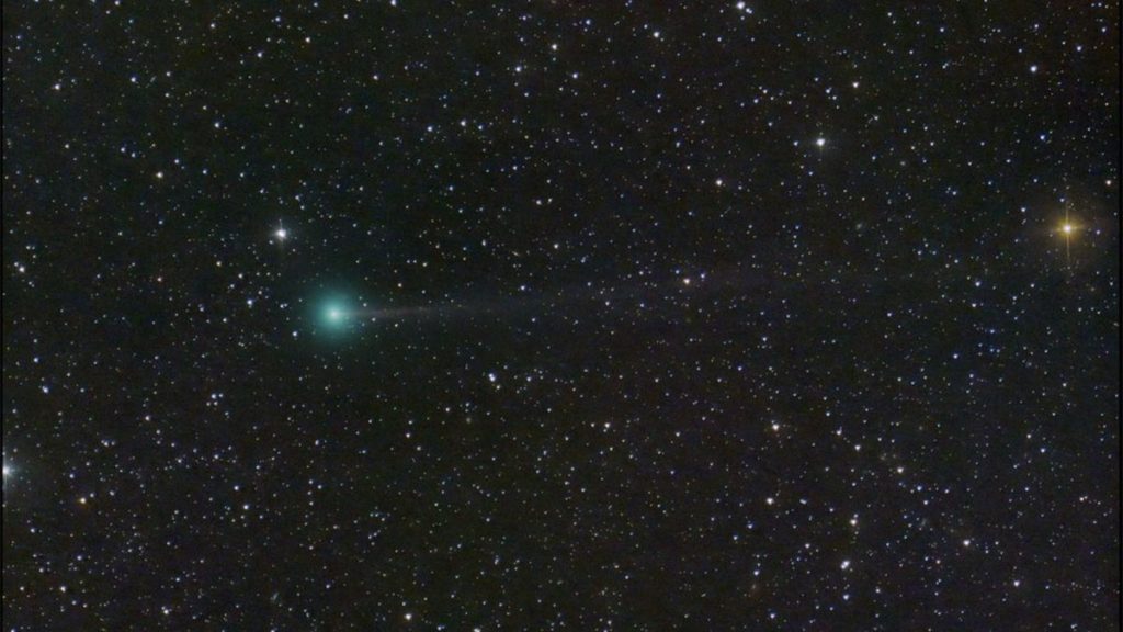 a green comet with a faint tail in the sky against a backdrop of stars