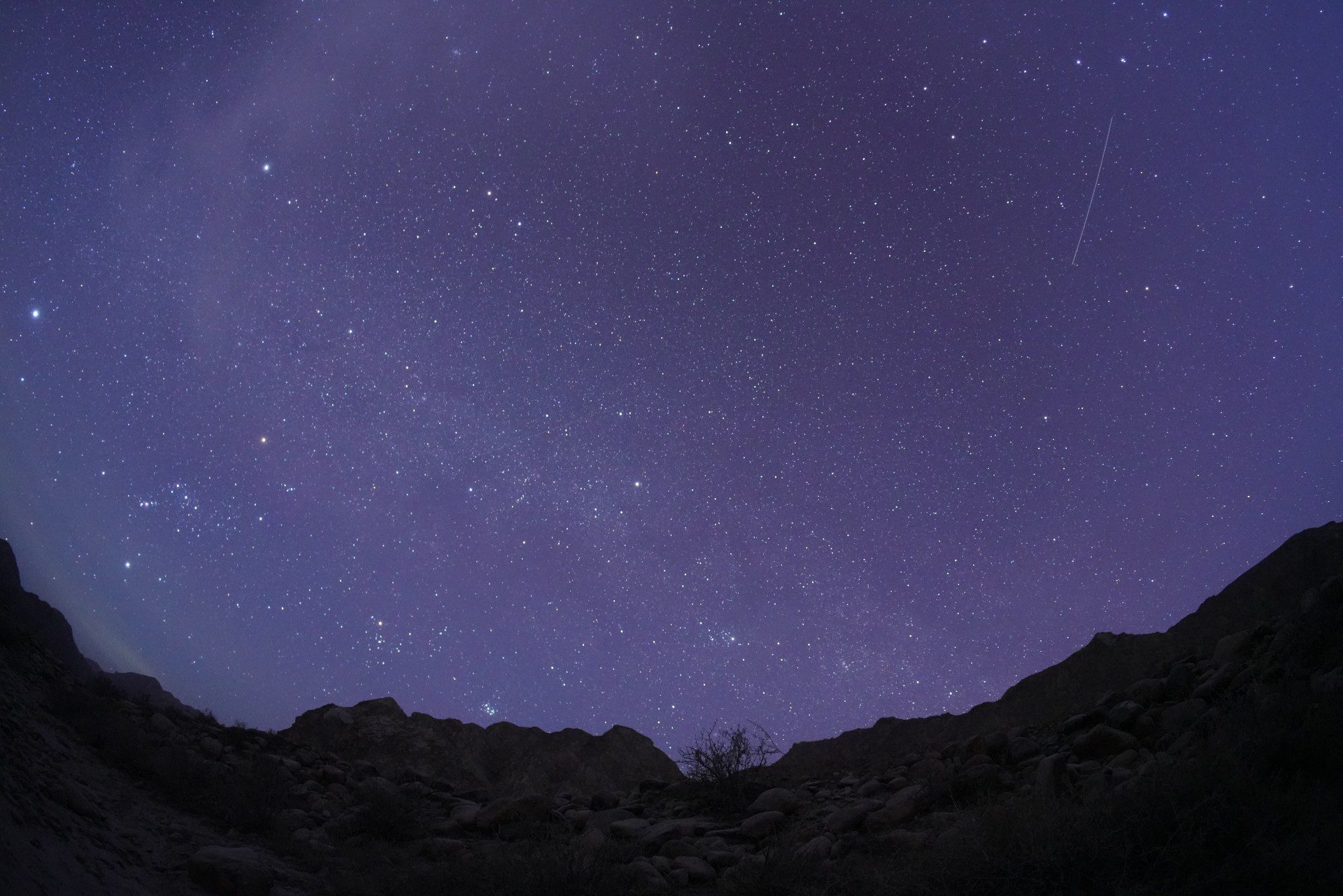 Een meteoor schiet door een sterrenhemel boven bergen