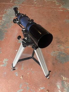 Een kleine telescoop wordt op een eenvoudige standaard op een betonnen vloer geplaatst